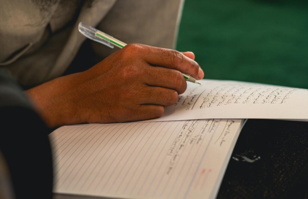 pexels-photo-28823666-28823666 Detailed view of a person's hand writing with a pen on paper in Arabic script.