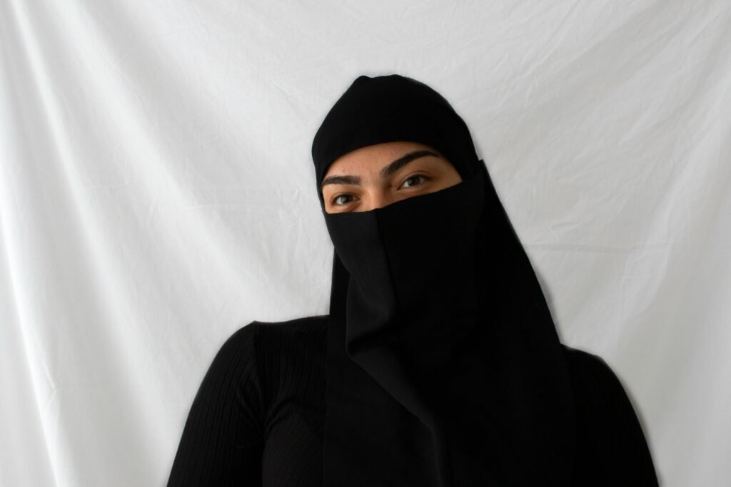 Close-up portrait of a woman wearing a black niqab against a white backdrop.