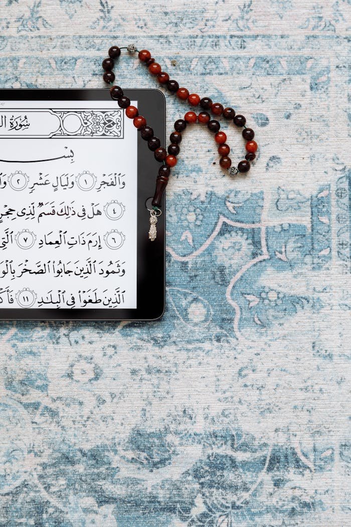 A tablet displaying the Quran on a prayer rug with prayer beads beside it.